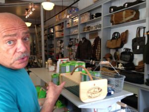 Mark Hodesh stands in Downtown Home & Garden pointing to some Filson bags.