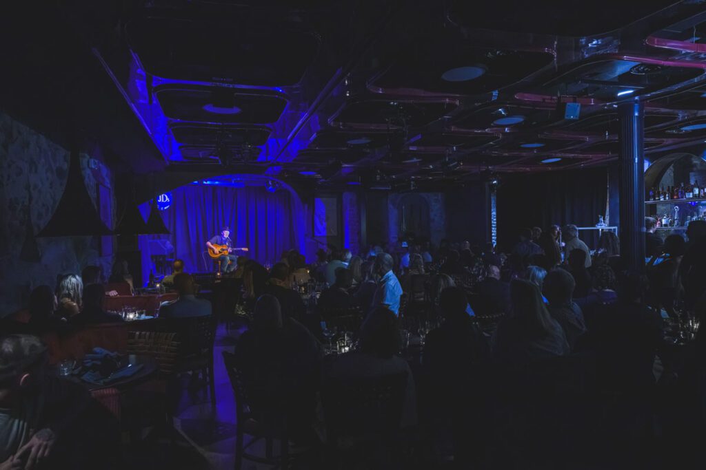 Jeff Daniels plays guitar onstage in a darkened music venue.
